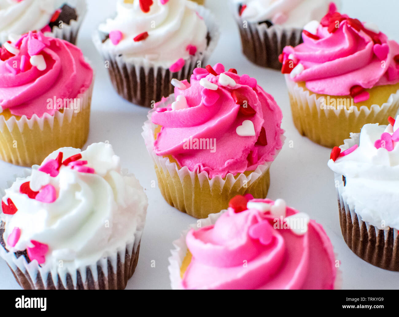 Valentine cupcakes con glaseado de colores rosa y blanco y corazón tropezones por encima Foto de stock