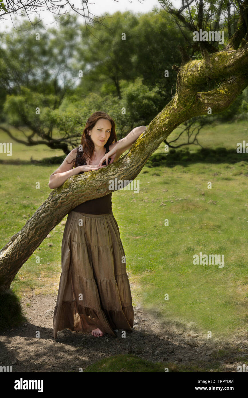 Mujer en una larga falda inclinada contra la rama de un árbol Foto de stock