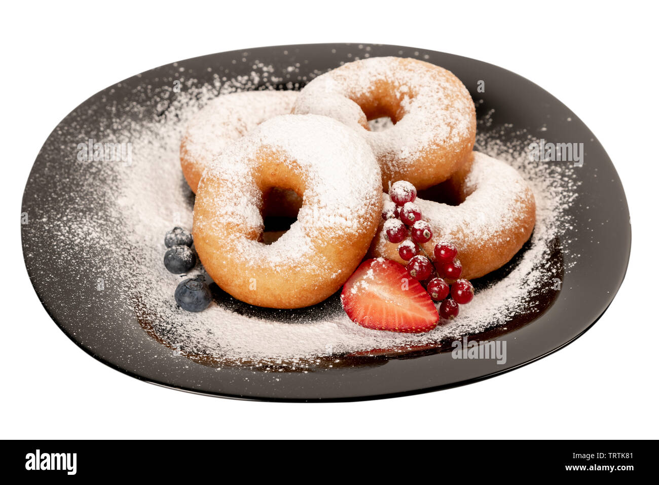 Jugoso donuts frescos cubiertos con azúcar en polvo sobre una placa negra con bayas sobre un fondo blanco aislado Foto de stock