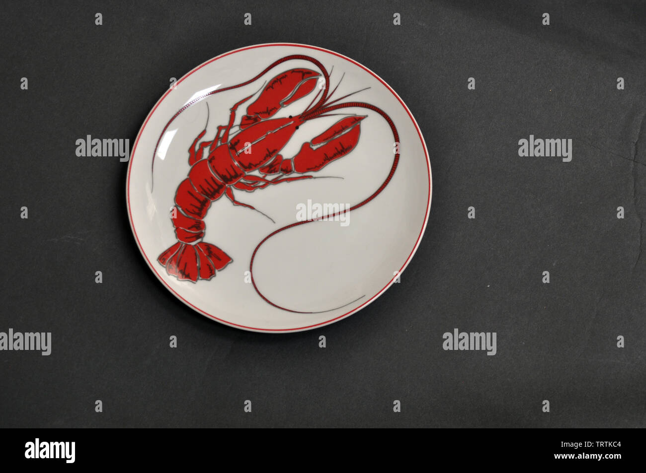 Plato de cena blanca redonda, con una imagen de langosta y ribetes rojos Foto de stock