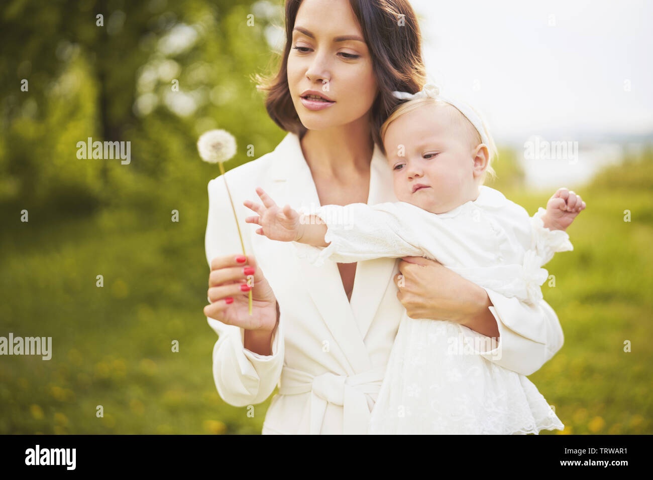 Outdoor retrato de moda joven hermosa madre e hija poco lindo soplando a jaramago sobre verde pradera. Imagen de primavera Foto de stock