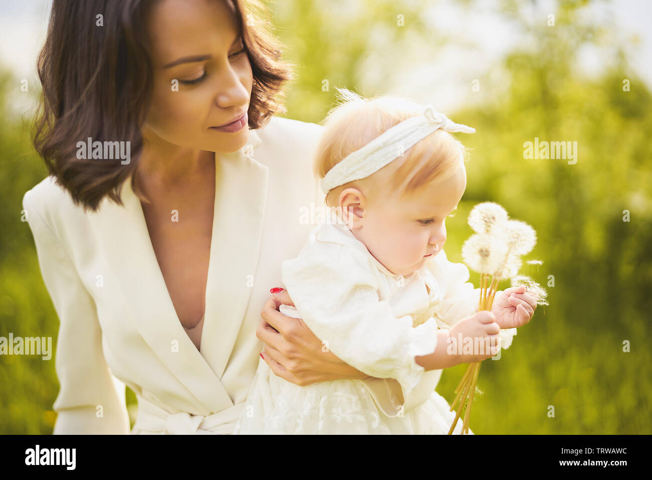 Outdoor retrato de moda joven hermosa madre e hija poco lindo soplando a jaramago sobre verde pradera. Imagen de primavera Foto de stock