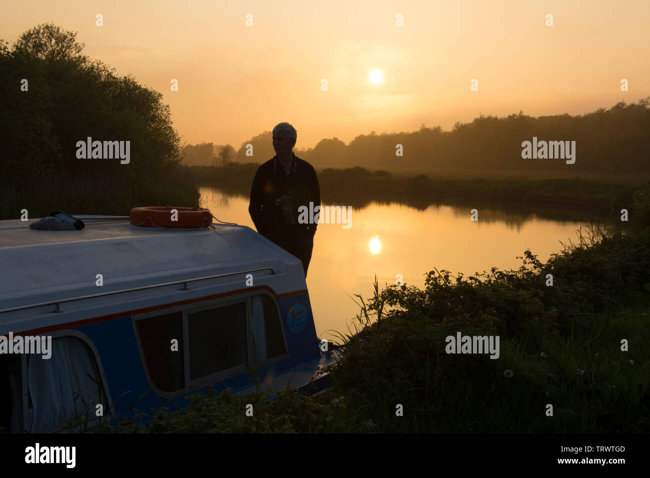 Hombre en vacaciones en la cubierta de una embarcación de recreo barco viendo una puesta de sol sobre el río Hormiga, los Norfolk Broads, REINO UNIDO, Mayo. Foto de stock