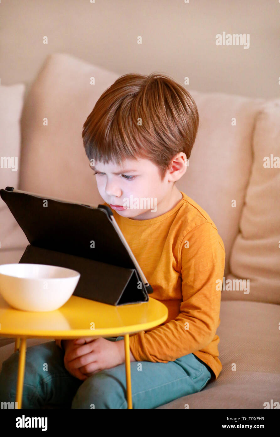 Niño con tablet PC en la cama, en su casa. El chico lindo sofá viendo  dibujos animados, jugar a juegos y aprendizaje desde el portátil. La  educación, la diversión, el ocio, la