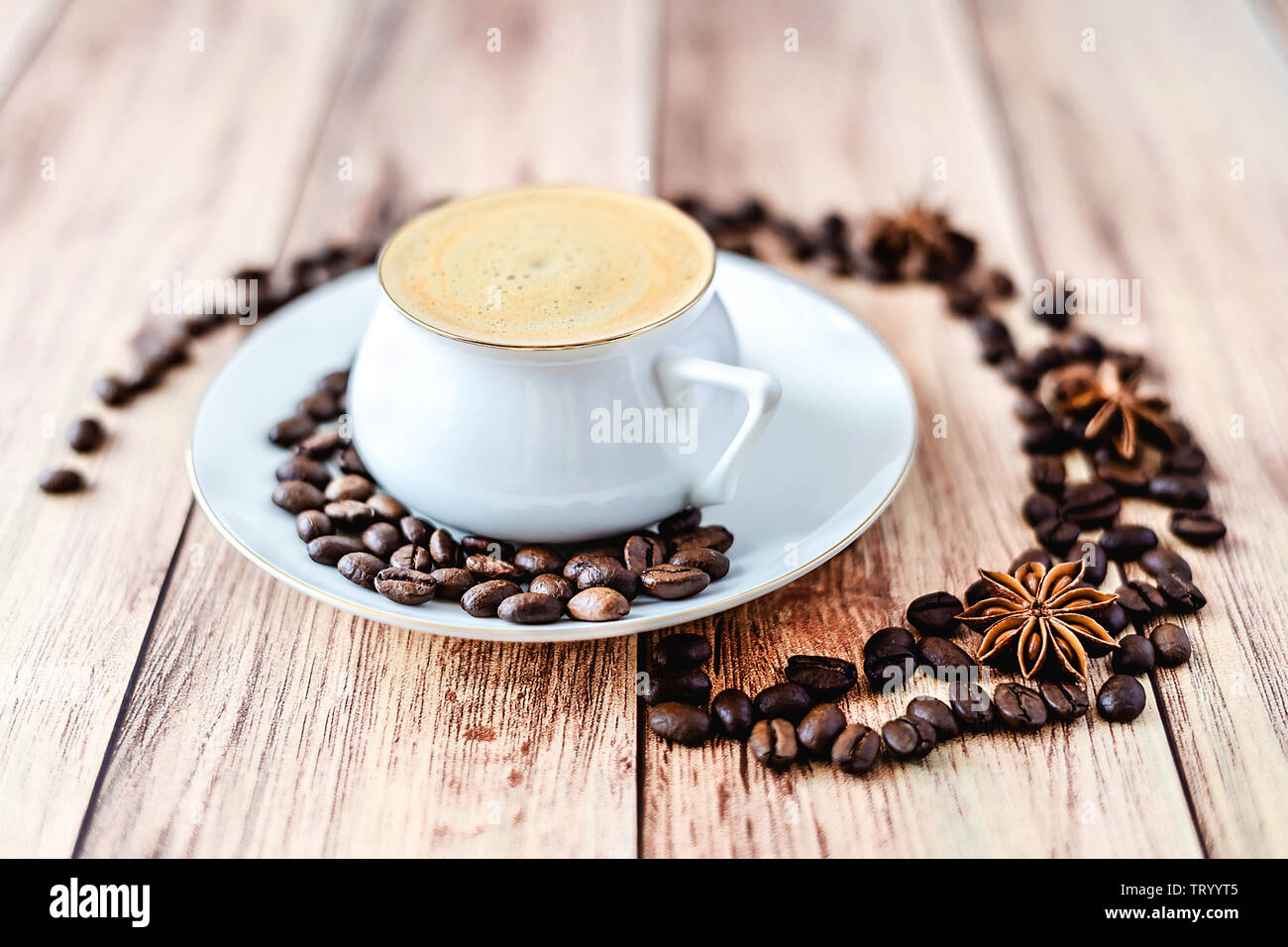 Vista cercana de una taza de café caliente sobre la mesa rústica de madera con granos de café derramado y anís. Espacio para el texto . Foto de stock