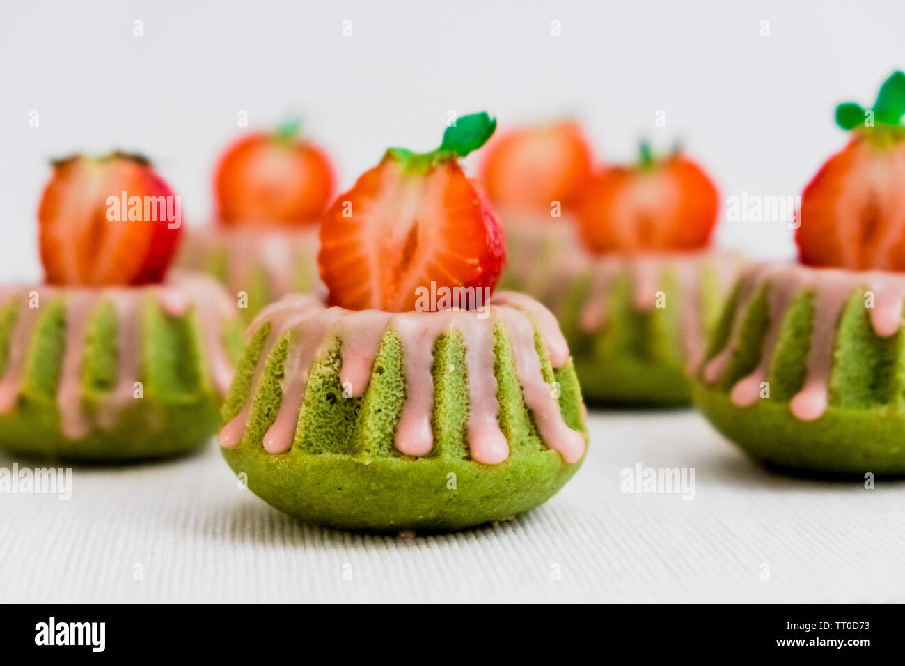 https://c8.alamy.com/compes/tt0d73/te-verde-matcha-mini-bundt-cakes-rociados-con-glaseado-de-fresa-y-cubierto-con-la-mitad-fresas-frescas-tt0d73.jpg