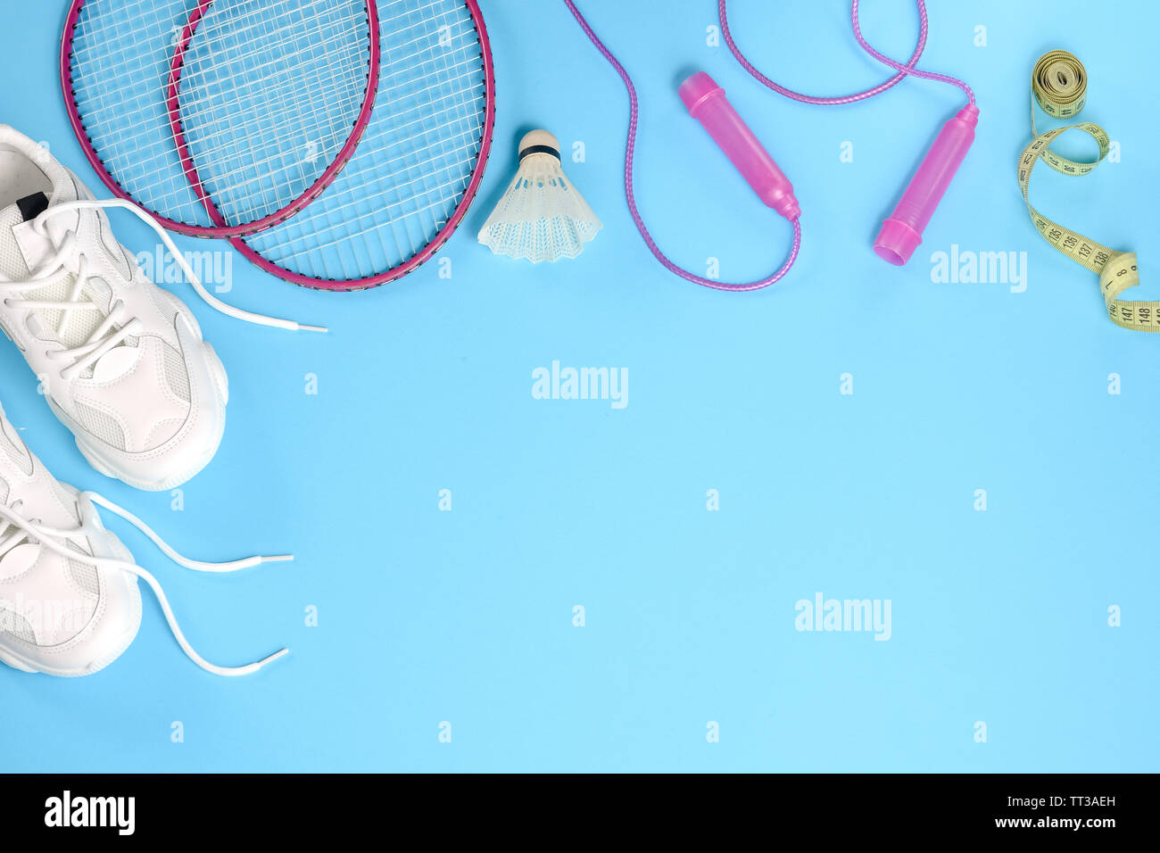 Deportes shuttlecock plana con laicos y badminton raqueta, comba, zapatillas y cinta métrica sobre fondo azul. Fitness, deporte y vida sana Foto de stock