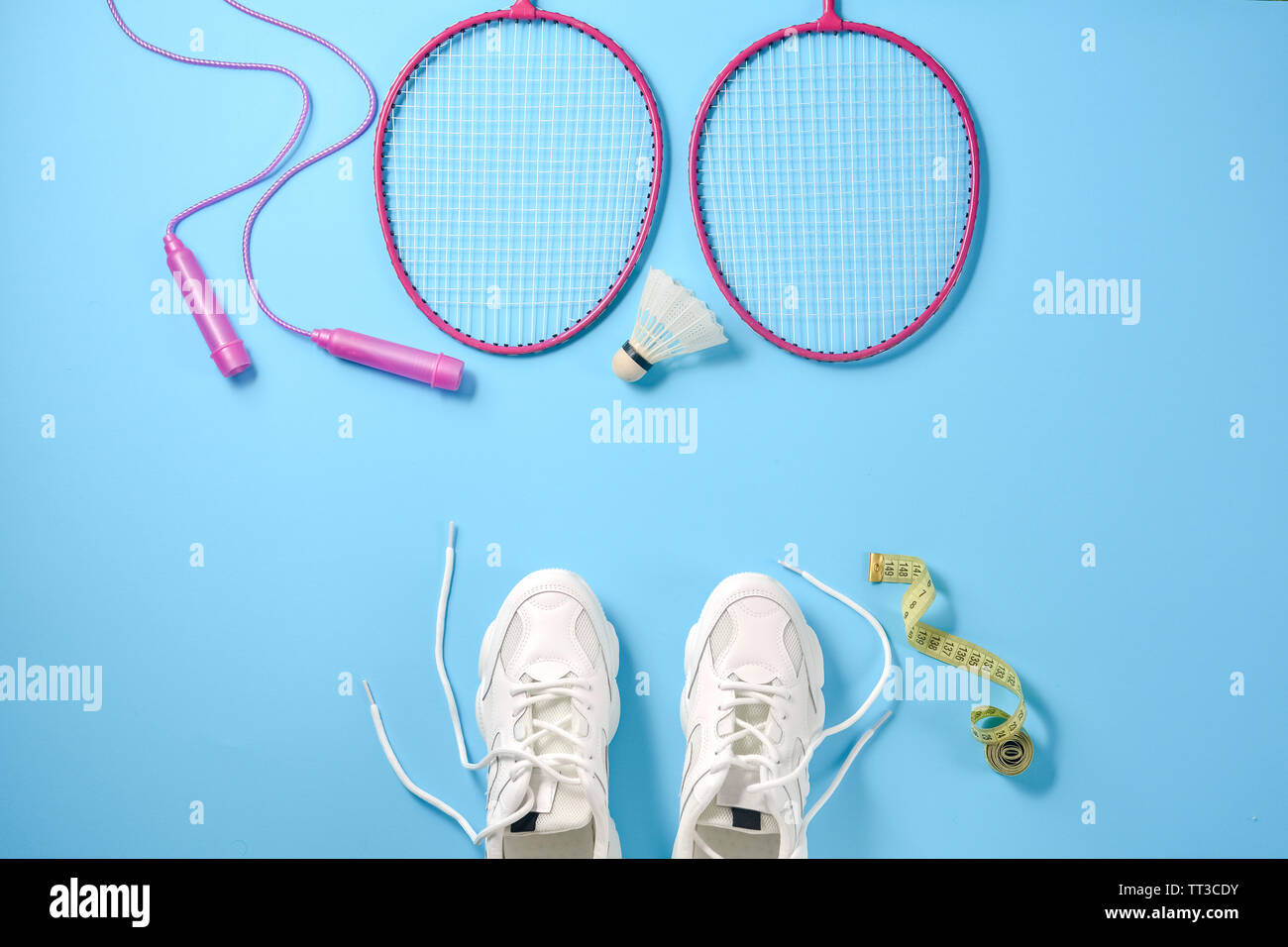 Deportes shuttlecock plana con laicos y badminton raqueta, comba, zapatillas y cinta métrica sobre fondo azul. Fitness, deporte y vida sana Foto de stock