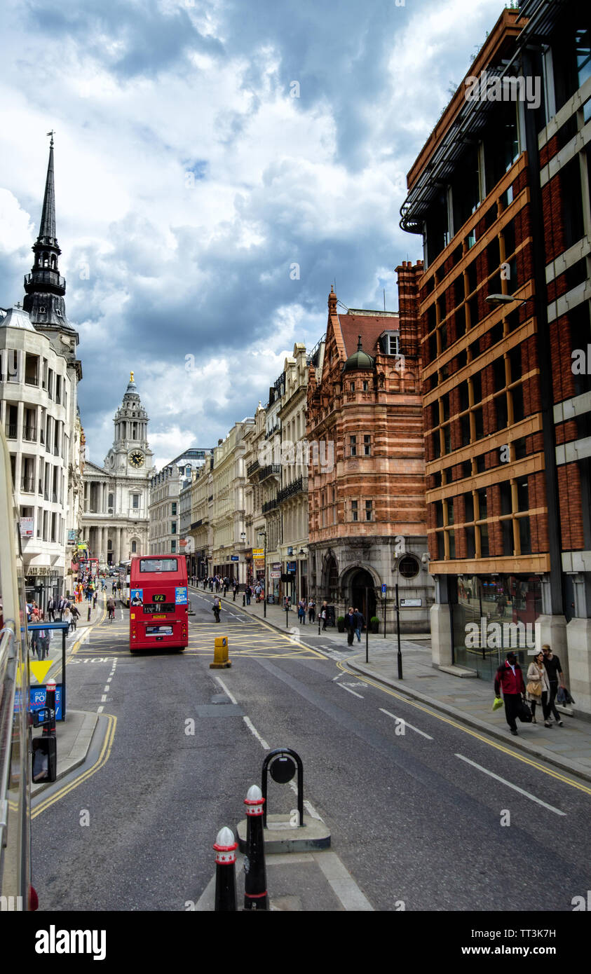 Autobuses rojos de Londres se está moviendo a través de una calle con edificios de arquitectura gótica en ambos lados. Foto de stock