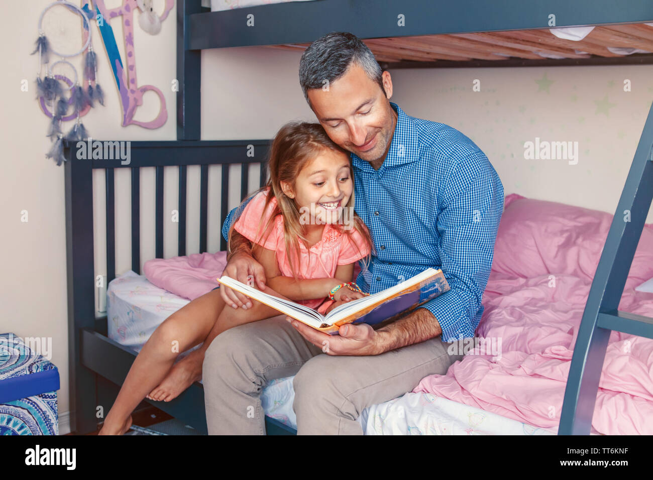 Dos personas de la familia sentada en la cama en el dormitorio libro de  lectura. Padre e hijas en casa chica pasar tiempo juntos. Hablando de padres  comunicar a chil Fotografía de