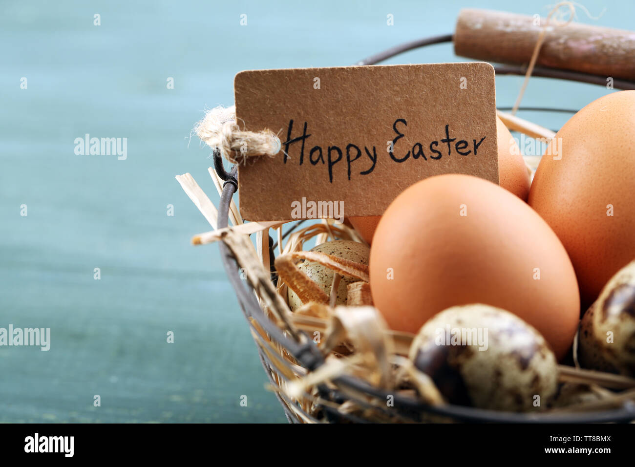 Huevos de aves en canasta de mimbre con flores decorativas en el color de fondo de madera Foto de stock