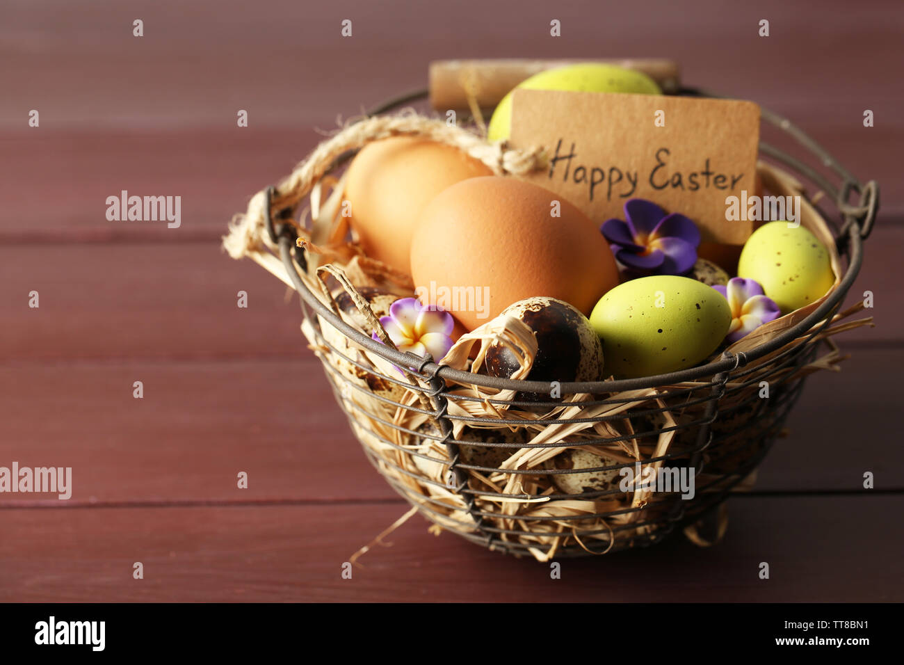 Huevos de aves en canasta de mimbre con flores decorativas en el color de fondo de madera Foto de stock