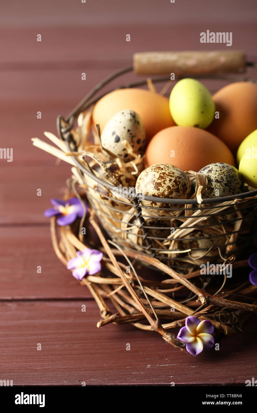 Huevos de aves en canasta de mimbre con flores decorativas en el color de fondo de madera Foto de stock