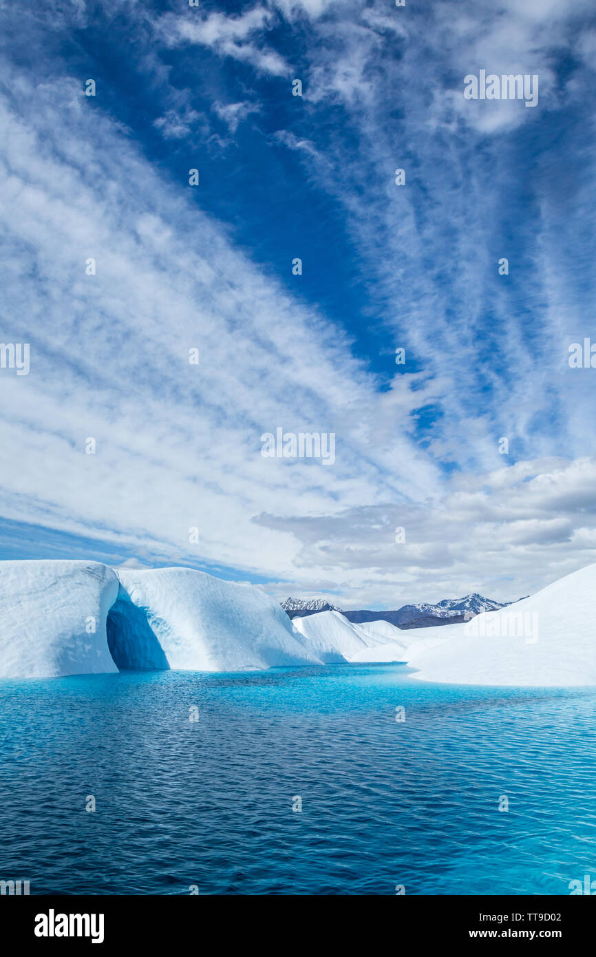 Las bandas de nubes de luz pasa sobre un lago de color azul profundo en el hielo del Glaciar Matanuska en Alaska. Una cueva de hielo también es visible en la parte izquierda, suelo Foto de stock