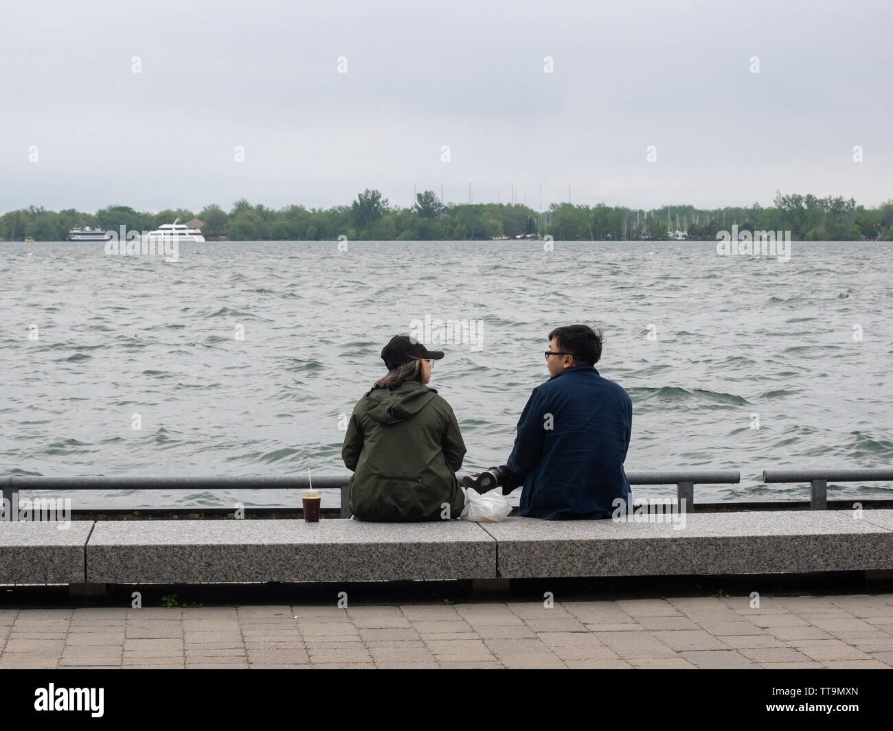 Toronto, Canadá. El 15 de junio, 2019. Dos personas disfrutando de una conversación en frente del puerto de Toronto, en un día nublado, ventoso. Foto de stock