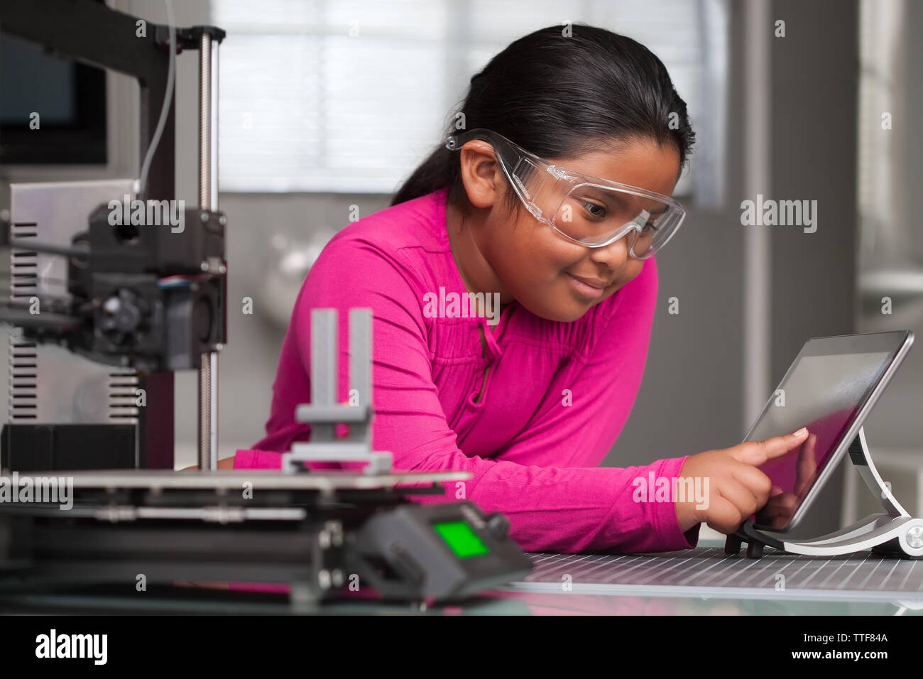 Un joven estudiante vestido rosa está trabajando en una pantalla táctil haciendo cambios a un juguete impresos en 3D en una escuela de verano de clase técnica. Foto de stock