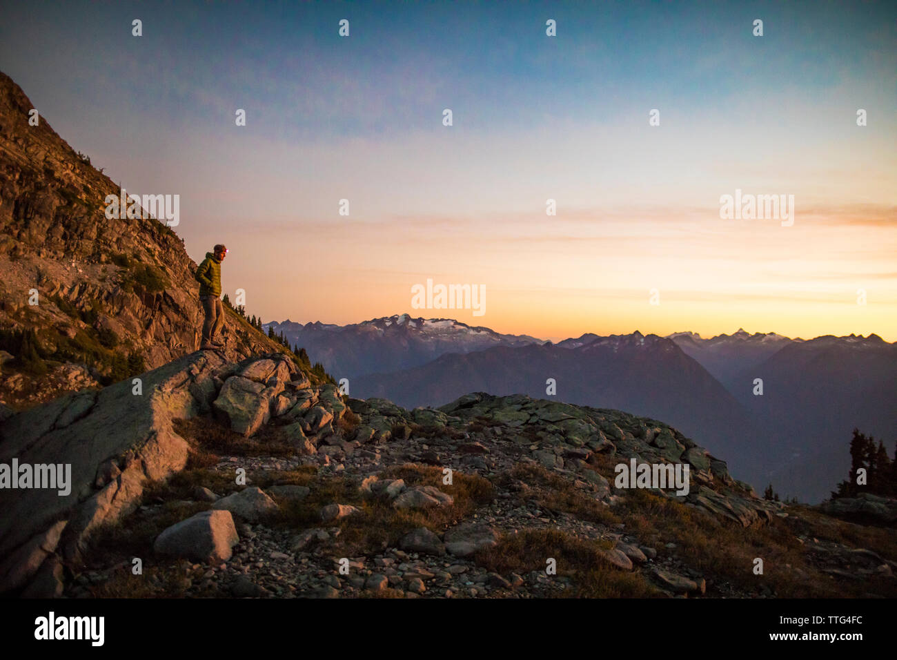 Montañero solitario parado sobre rock bluff en las montañas al atardecer. Foto de stock