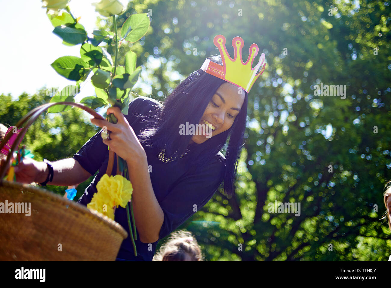 Feliz mujer vistiendo la corona de papel mientras llevaba la canasta durante Fiesta de cumpleaños en el patio Foto de stock