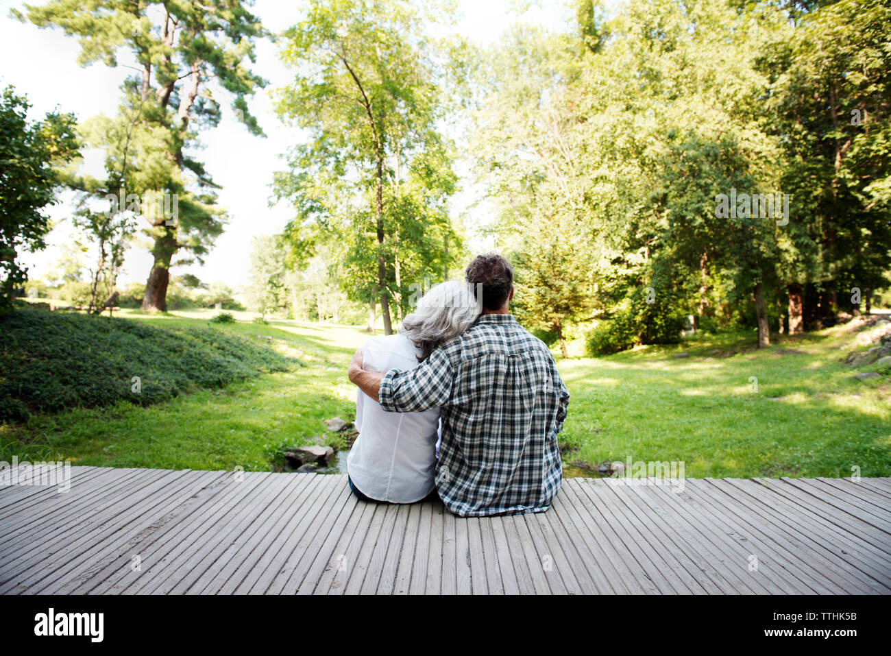 Vista trasera de la pareja sentada con brazo alrededor en el porche Foto de stock
