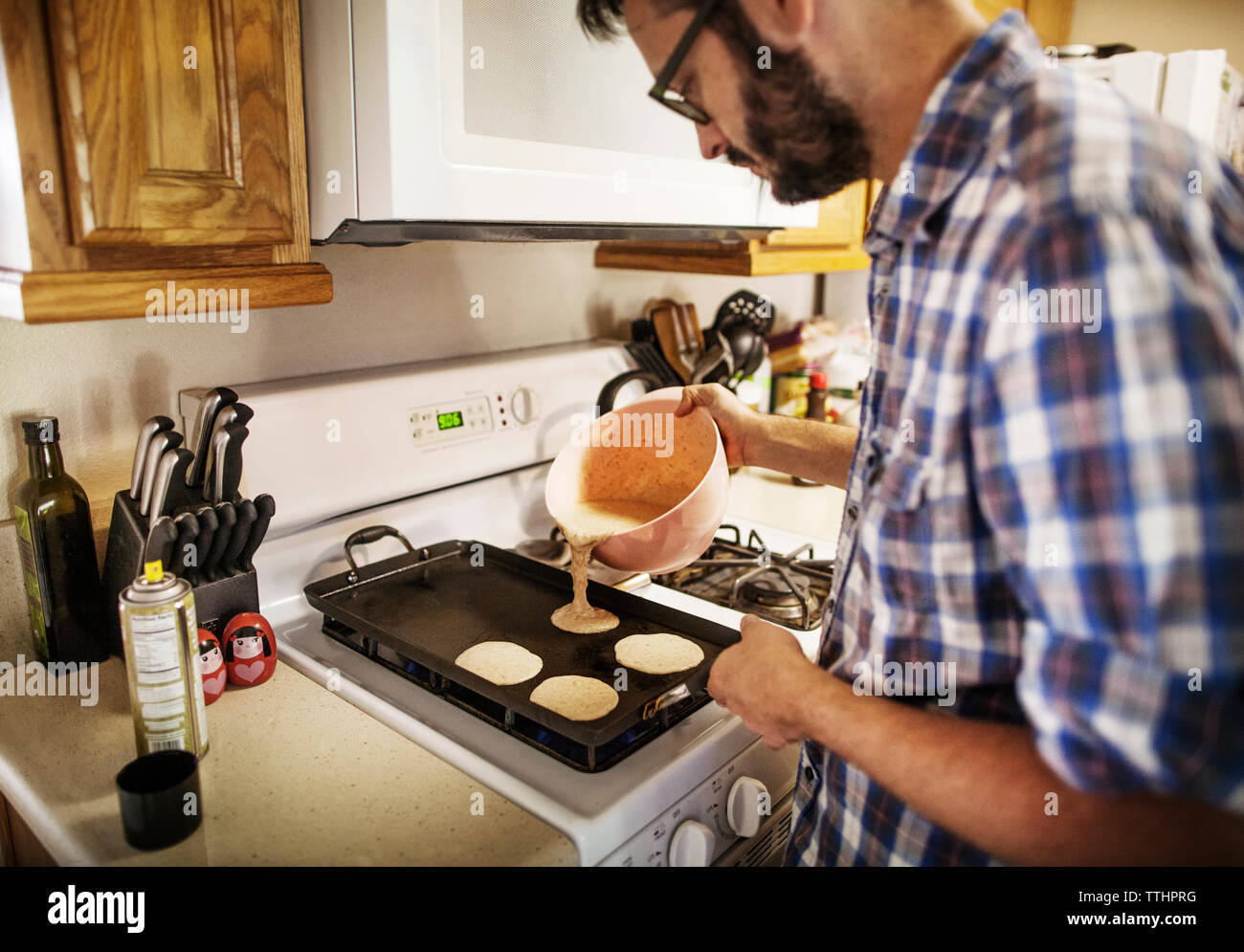 Hombre vertiendo pan masa para tartas en la hoja de hornear en casa Foto de stock