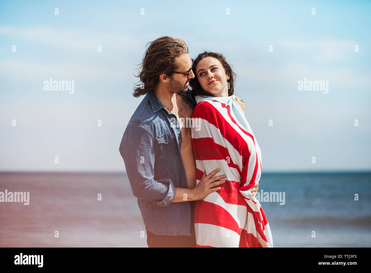 Vista lateral del pie con mujer hombre romántico envuelto en una manta en la playa Foto de stock