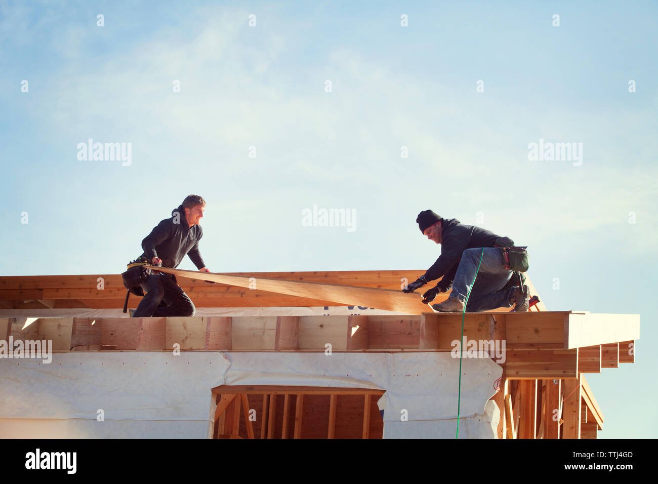 trabajadores que construyen vigas de techo contra el cielo durante el día soleado Foto de stock