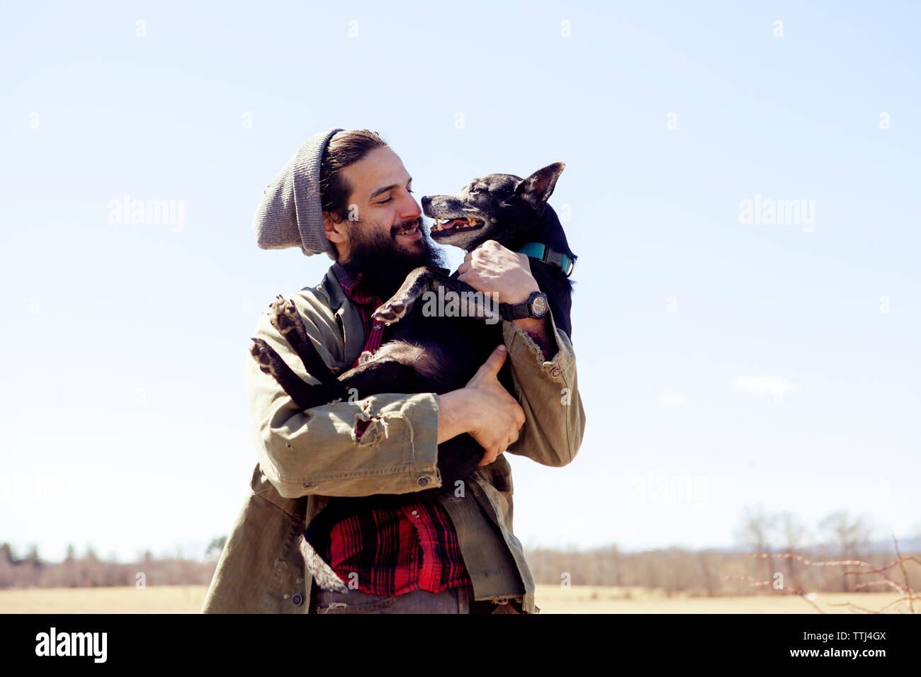Feliz el hombre lleva perro mientras está de pie contra el cielo claro Foto de stock