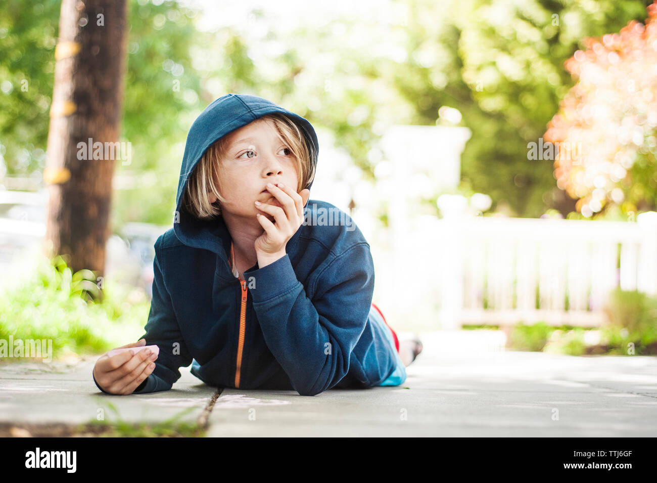 Niño sosteniendo chalk tumbado en la acera Foto de stock