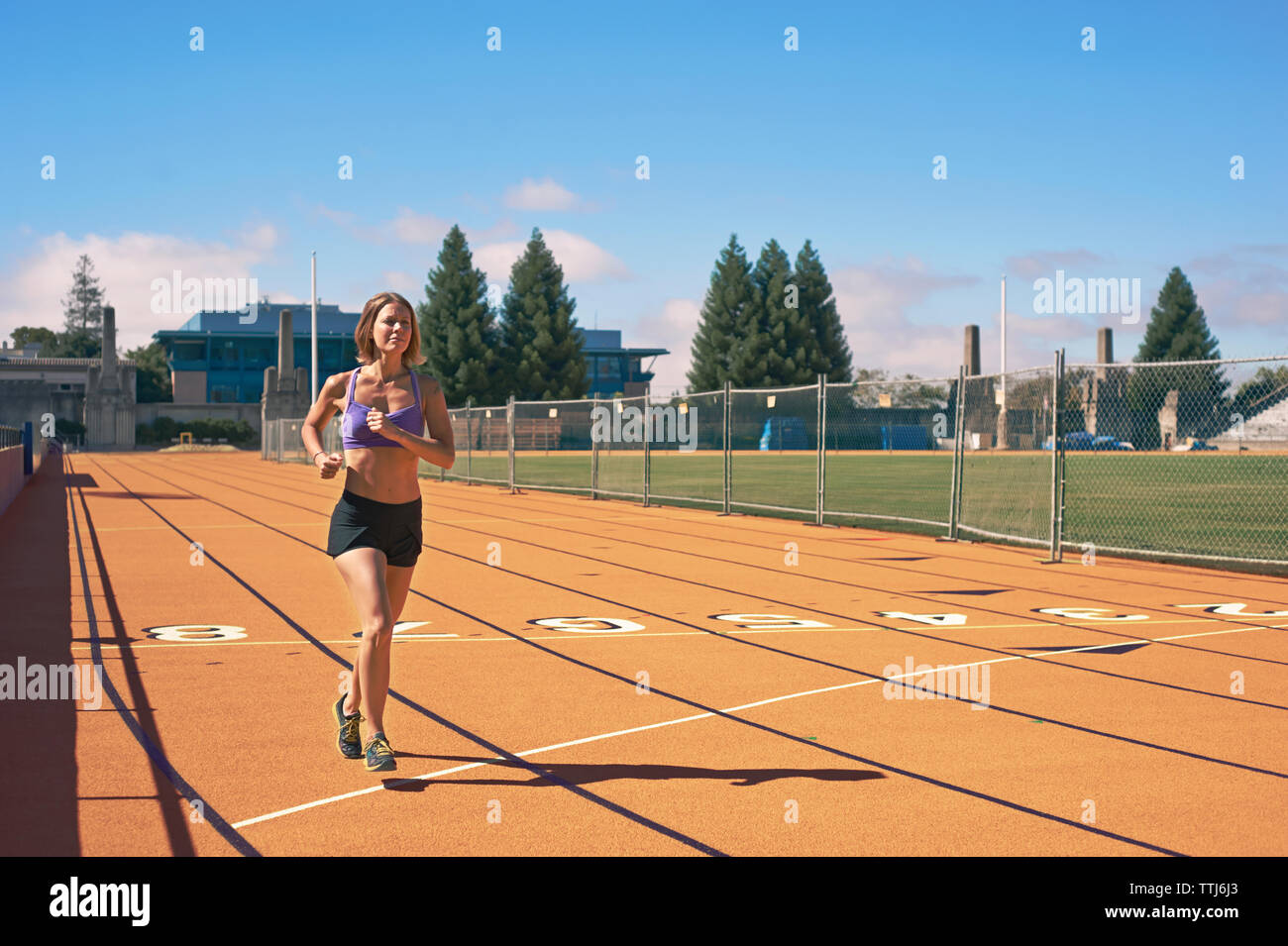 Ejecutando la atleta femenina en la vía contra el cielo Foto de stock