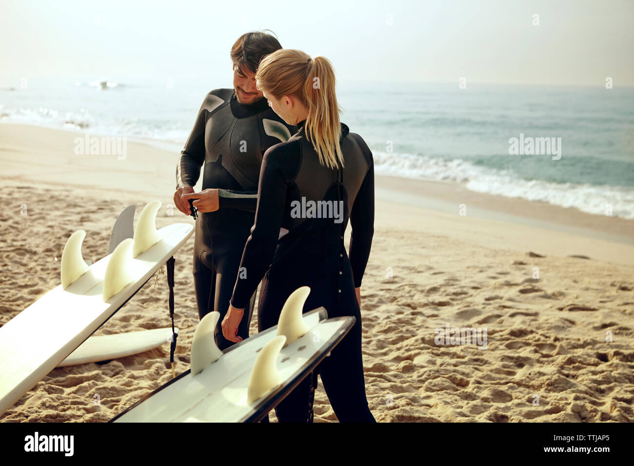 El hombre apuntando a la tabla de surf mientras está de pie por la mujer en la playa Foto de stock