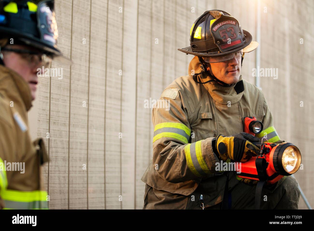 El bombero sosteniendo la linterna mientras compañero mirando lejos Foto de stock
