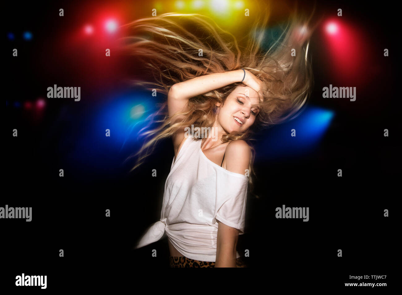 Mujer con cabello rubio bailando contra encendido luces multicolores en garden party Foto de stock