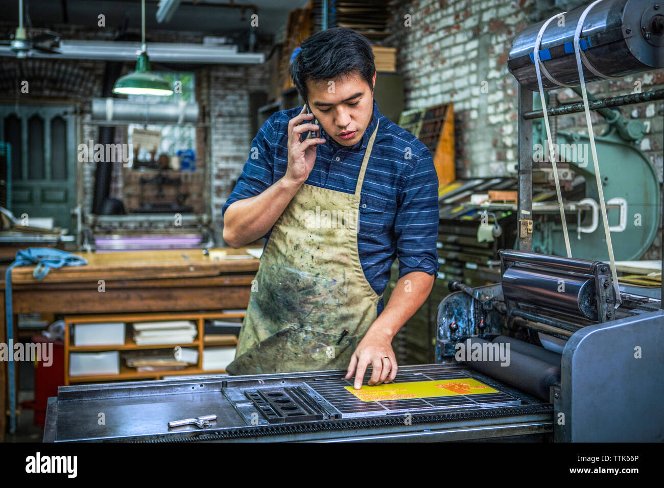 Hombre utilizando el teléfono móvil mientras está de pie de imprenta en el taller Foto de stock