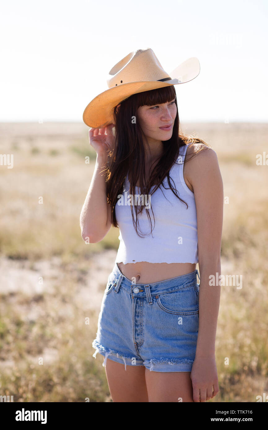 Mujer vistiendo sombrero de cowboy mirando a otro lado mientras está parado  en el campo Fotografía de stock - Alamy
