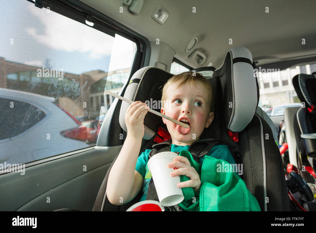 Chico lindo lamiendo paja para beber mientras está sentado en el asiento del vehículo en alquiler Foto de stock