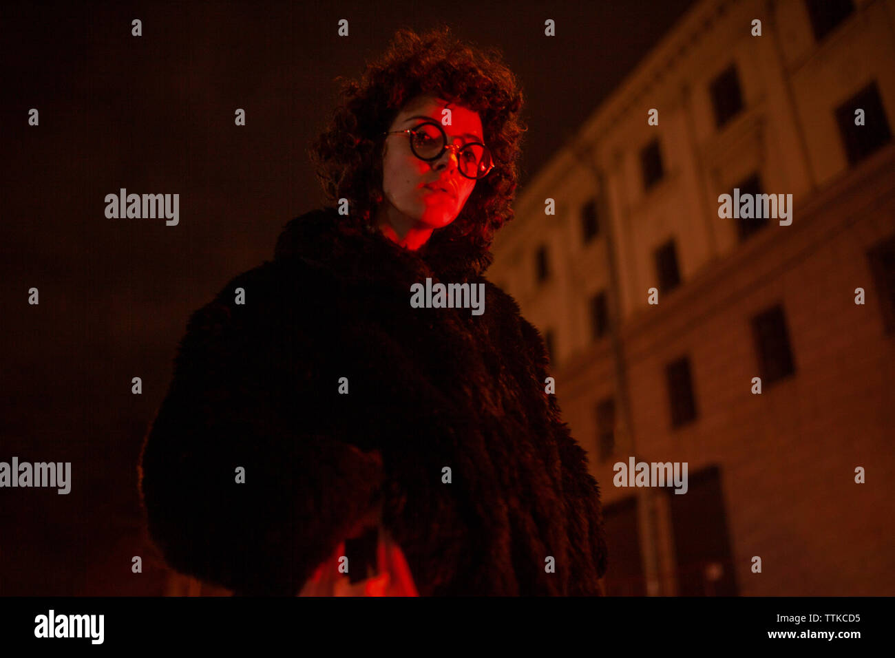 Rizado mujer en un abrigo de pieles en la noche iluminada con luz roja Foto de stock