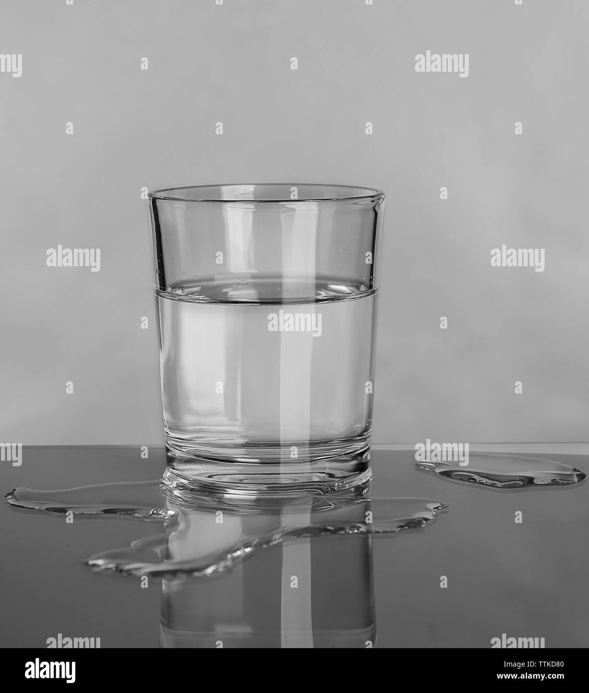 Vidrio y derramado agua sobre fondo gris Foto de stock