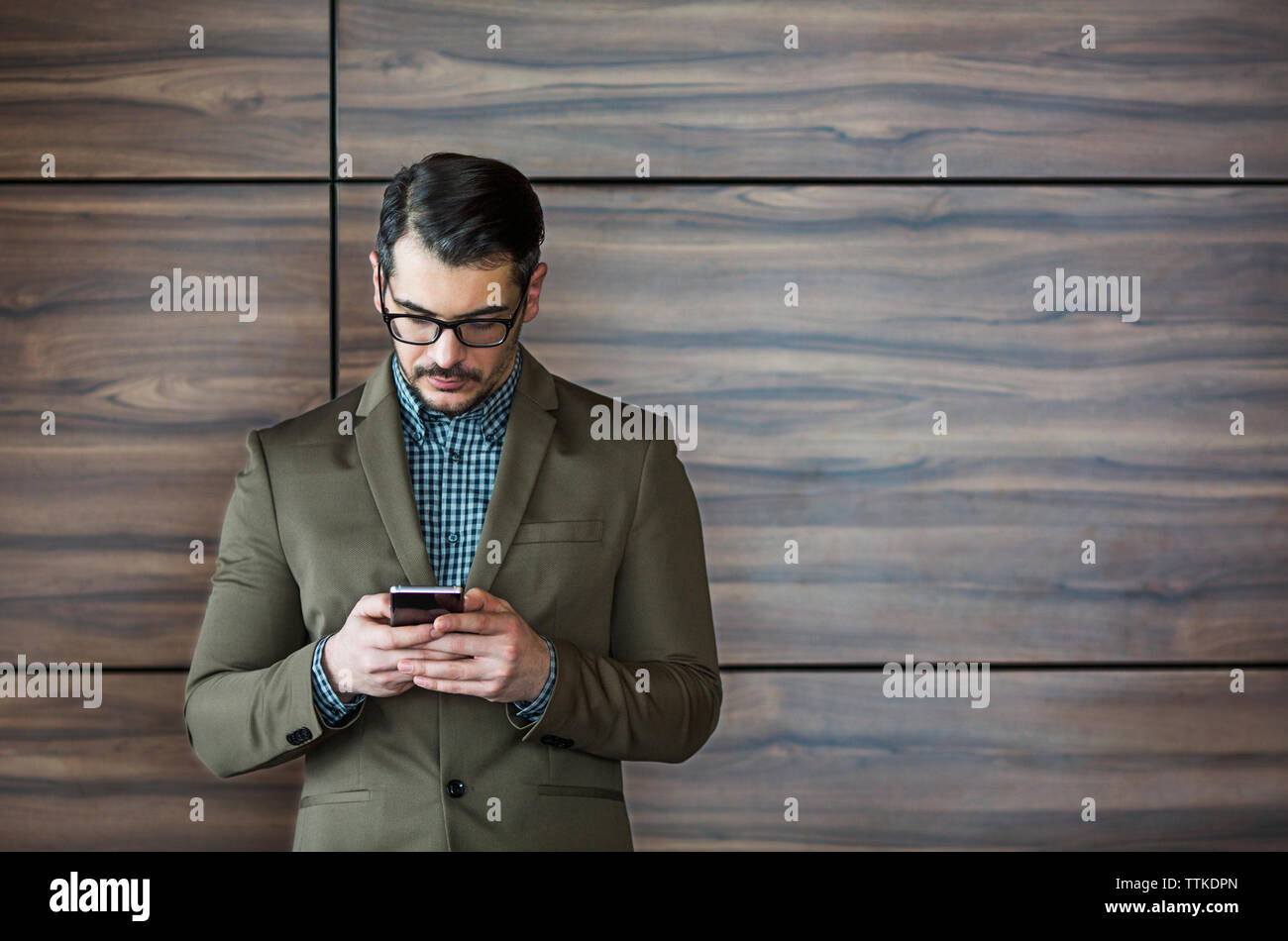 Empresario utilizando smart phone mientras está de pie contra la pared de madera Foto de stock