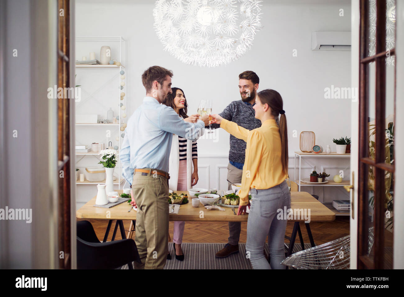 Amigos elevando brindis de celebración mientras está de pie en una mesa para comer en el almuerzo parte Foto de stock