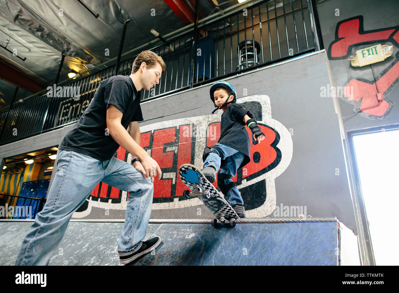 Joven se prepara para caer en una rampa de skate con ayuda del instructor Foto de stock