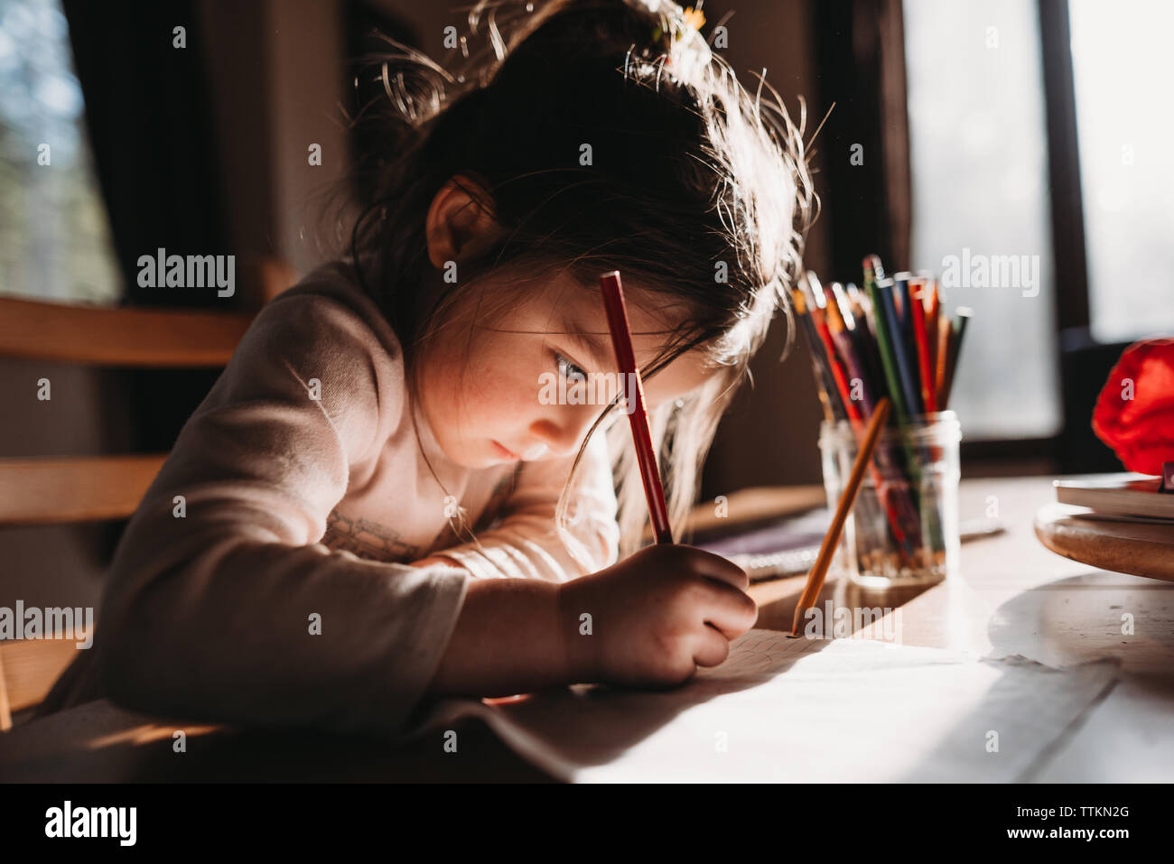 Chica de dibujo con lápices de colores sobre papel mientras está sentado en la mesa Foto de stock