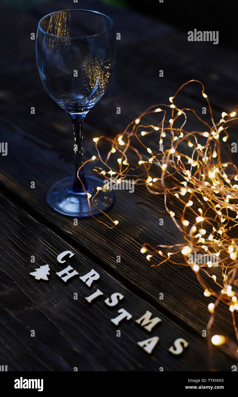 Un alto ángulo de visualización de cadena iluminado con luces de Navidad wineglass y texto en tabla de madera Foto de stock