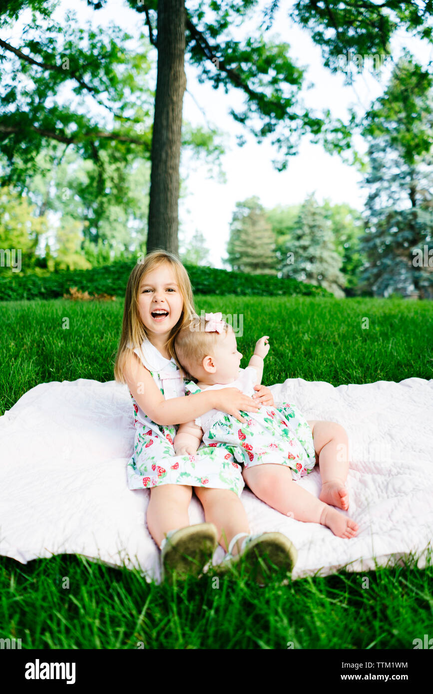 Una niña ríe mientras sostiene que su hermana de bebé Foto de stock