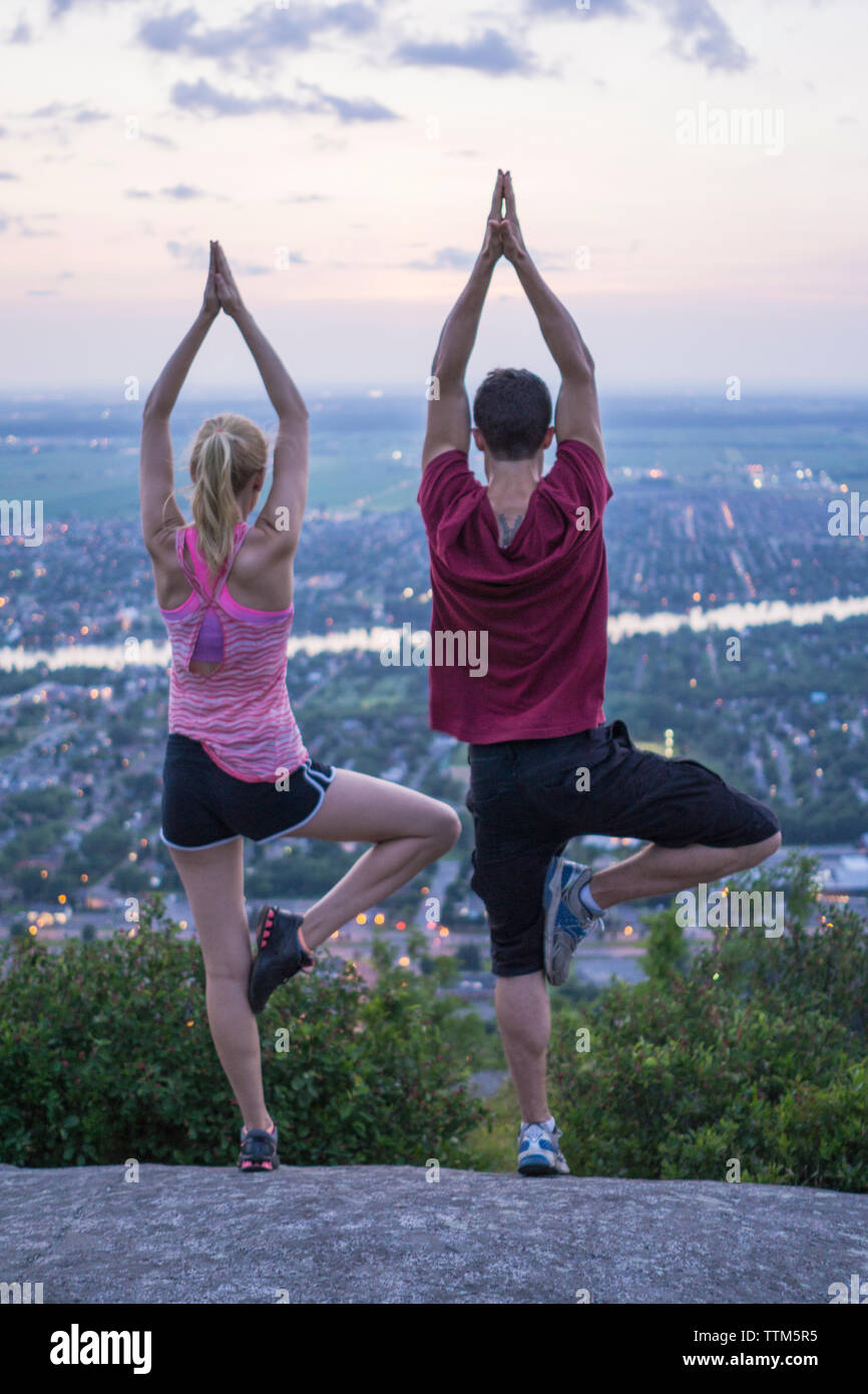 Par hacer yoga juntos en la cima de una montaña durante la puesta de sol en el este de Canadá Foto de stock
