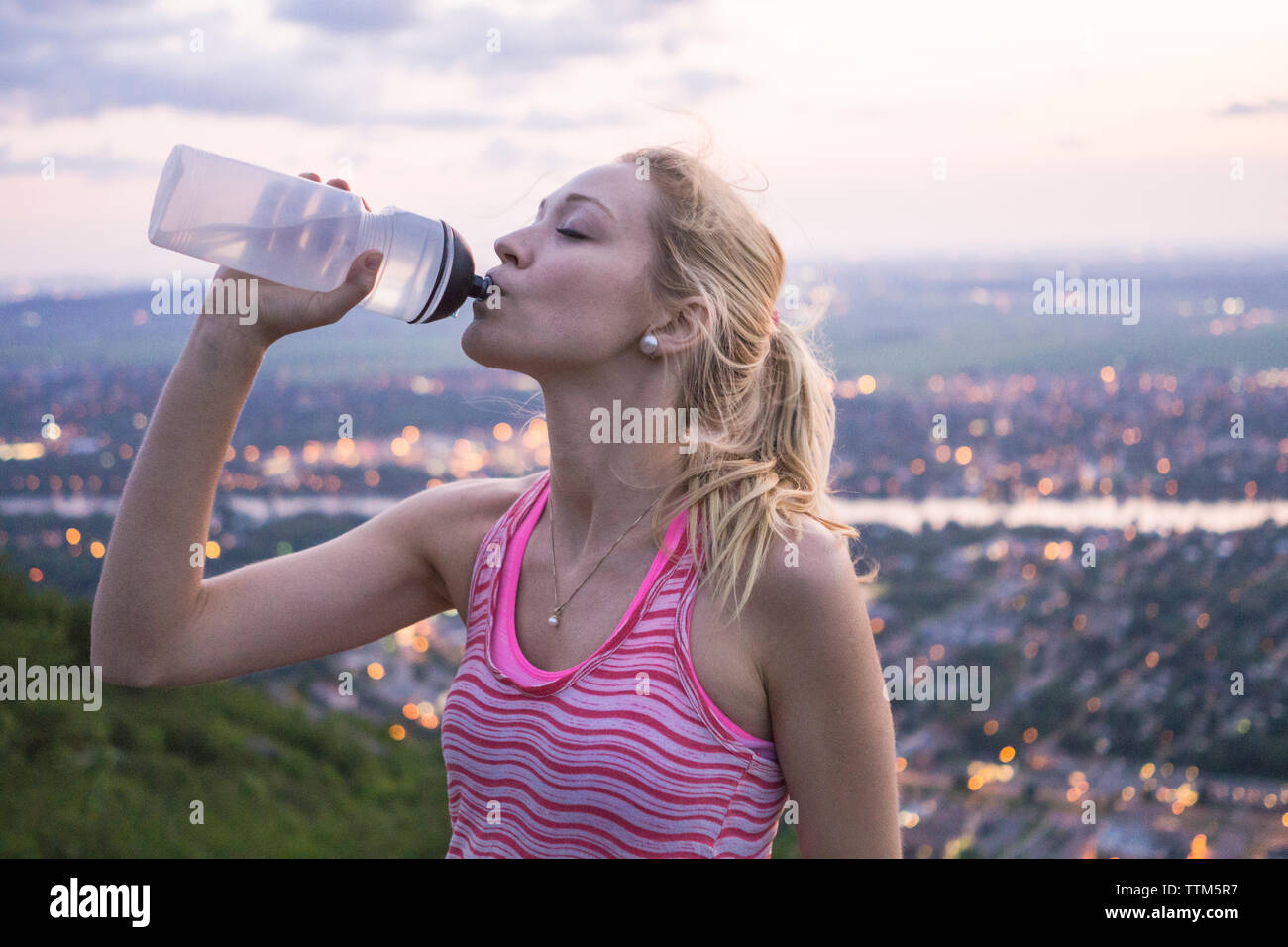 Excursionista hembra beber agua de botella reutilizable en la cima de la montaña durante la tarde caminata en el este de Canadá Foto de stock