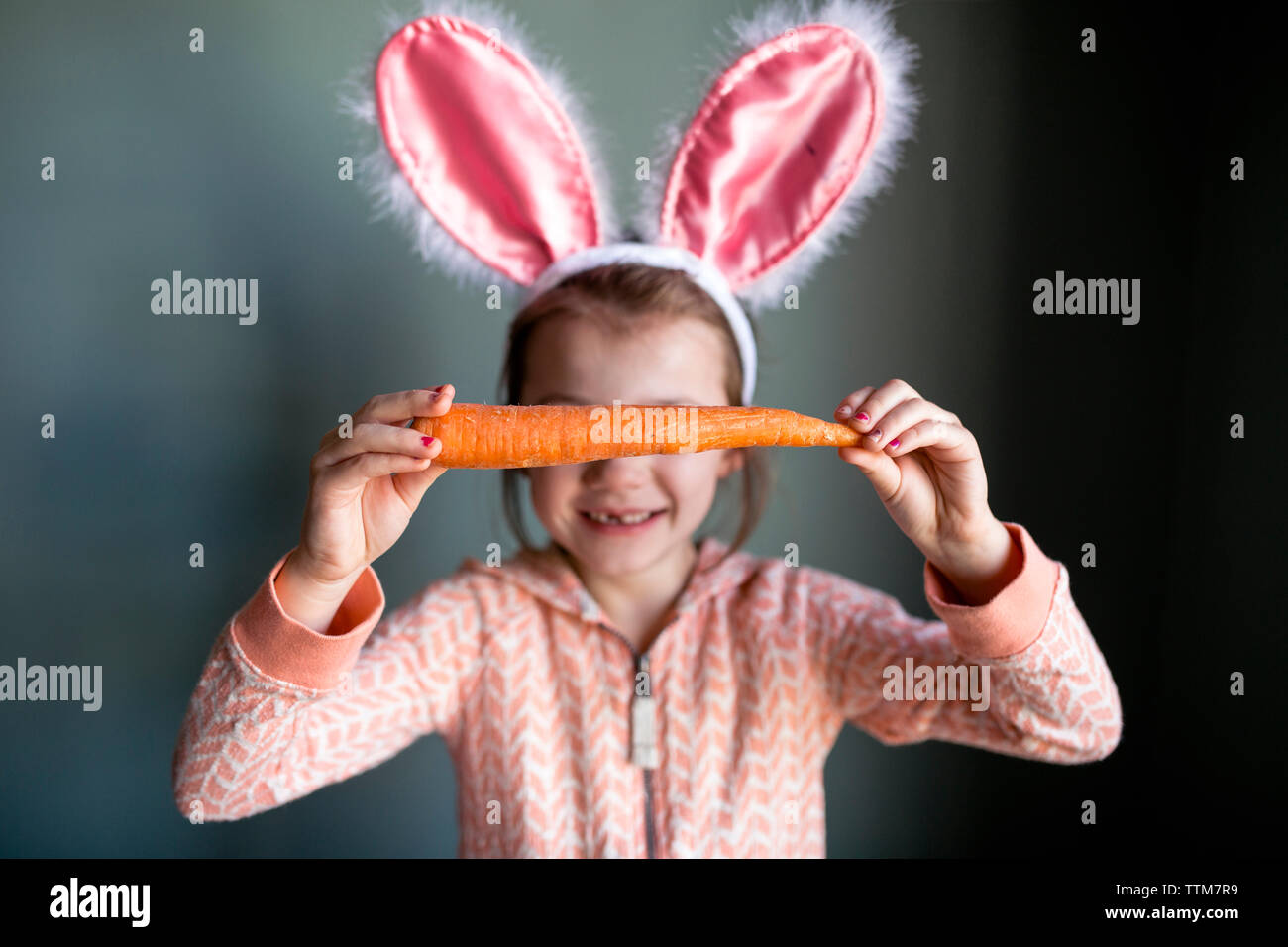 Juguetón vestida de diadema orejas de conejo mientras mantiene la zanahoria en casa Foto de stock
