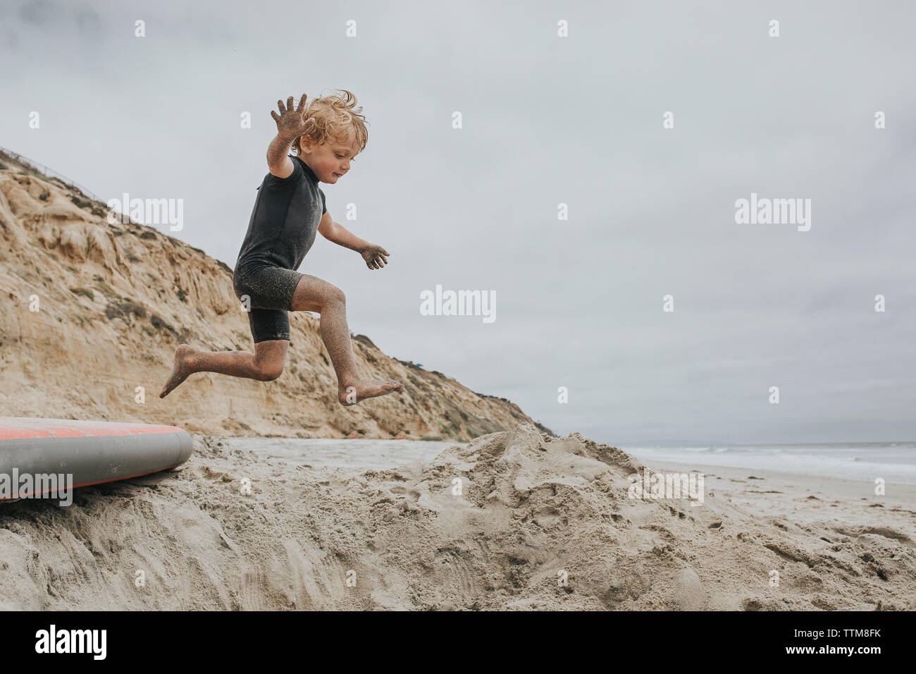 Muchacho juguetón saltando sobre la arena en la playa Foto de stock