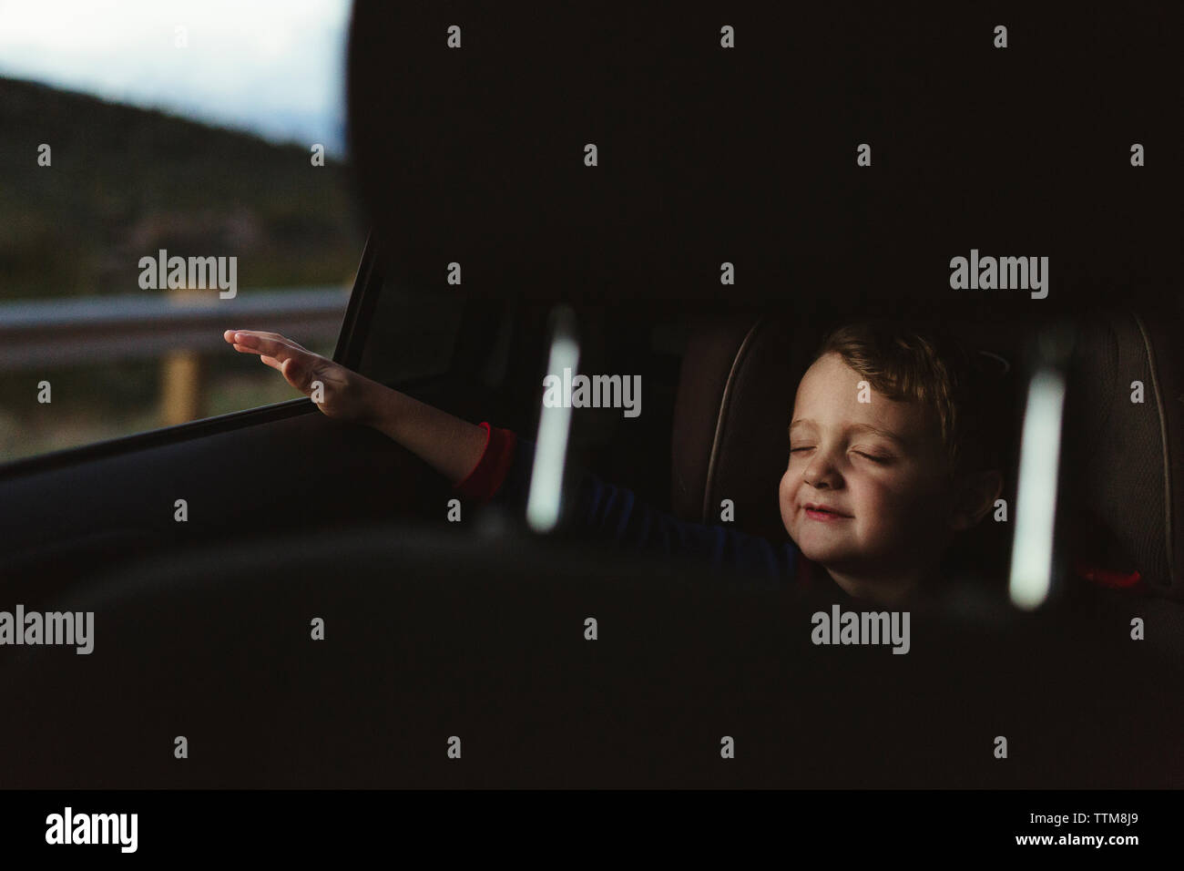 Chico lindo con los ojos cerrados disfrutando de road trip vistos a través de asiento del vehículo. Foto de stock