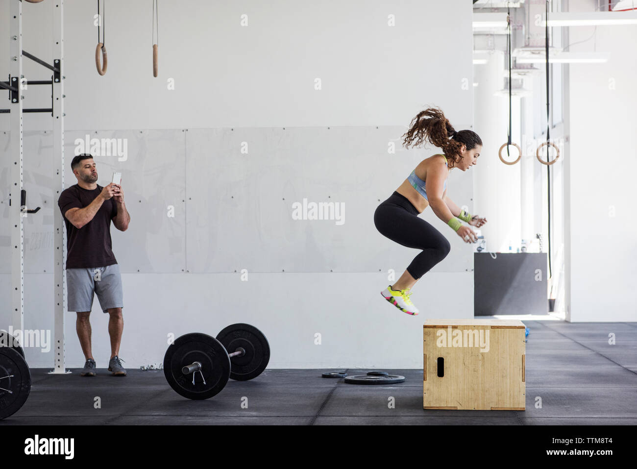Instructor fotografiar deportista ejercer sobre el cuadro saltar en el gimnasio crossfit Foto de stock