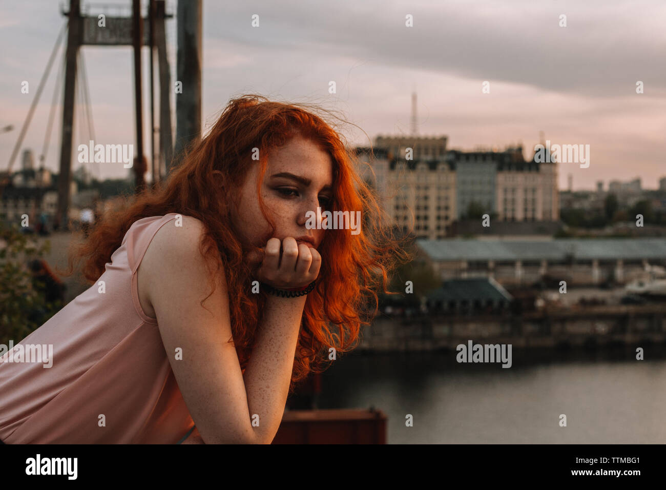 Retrato de niña de cabello rojo reflexivo apoyado en la baranda de puente Foto de stock